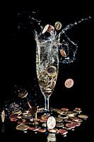Money coins fall into a champagne glass against a black background