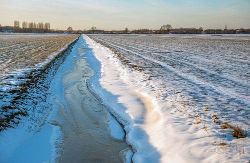 Bevroren sloot in besneeuwd Nederlands landschap