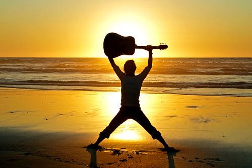 Gitaar muzikant op het strand met zonsondergang
