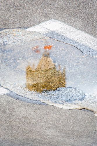 De top van de Domtoren in Utrecht weerspiegeld in een plas.