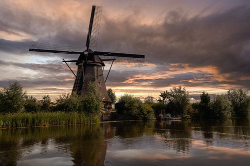 Zonsondergang met molen aan water.